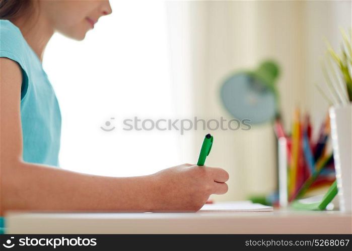 people, children and education concept - happy girl writing to notebook at home. happy girl writing to notebook at home