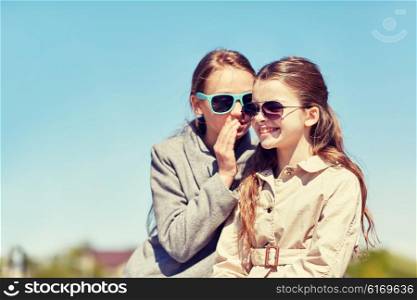 people, children and friendship concept - happy little girl in sunglasses whispering her secret to friends ear or gossiping outdoors