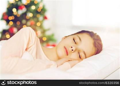 people, children and holidays concept - girl sleeping in bed over christmas tree background. girl sleeping in bed over christmas tree