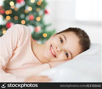 people, children and holidays concept - happy smiling girl lying awake in bed at christmas. happy smiling girl lying awake in bed at christmas