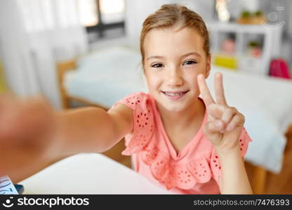 people, children and technology concept - girl taking selfie at home. happy girl taking selfie at home
