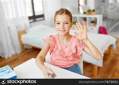 people, children and technology concept - girl taking selfie with monopod and waving hand at home. happy girl taking selfie and waving hand at home