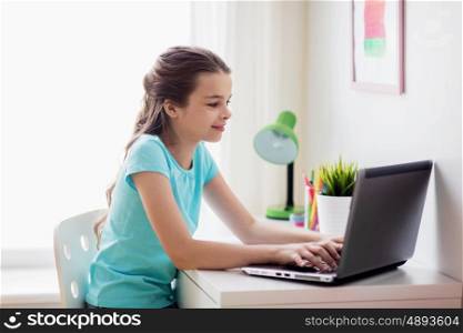 people, children and technology concept - girl typing on laptop computer at home