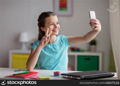 people, children and technology concept - girl with laptop computer and smartphone taking selfie or having video call at home. happy girl with smartphone taking selfie at home
