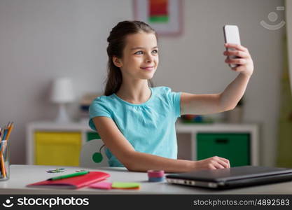 people, children and technology concept - girl with laptop computer and smartphone taking selfie at home