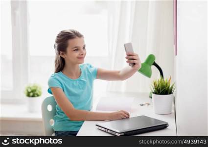 people, children and technology concept - girl with laptop computer and smartphone taking selfie at home. happy girl with smartphone taking selfie at home