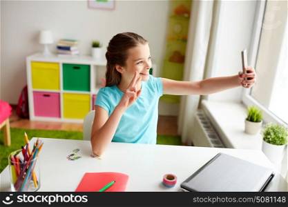 people, children and technology concept - girl with laptop computer and smartphone taking selfie at home. happy girl with smartphone taking selfie at home