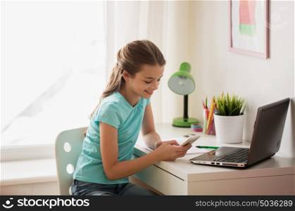 people, children and technology concept - girl with laptop computer and smartphone texting at home. girl with laptop and smartphone texting at home
