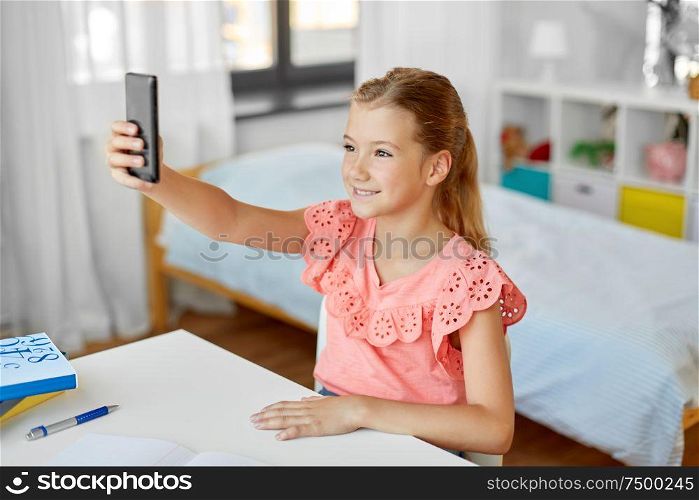 people, children and technology concept - girl with smartphone taking selfie at home. happy girl with smartphone taking selfie at home