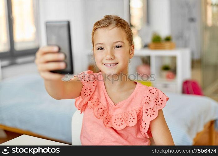 people, children and technology concept - girl with smartphone taking selfie at home. happy girl with smartphone taking selfie at home
