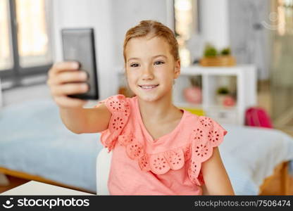 people, children and technology concept - girl with smartphone taking selfie at home. happy girl with smartphone taking selfie at home