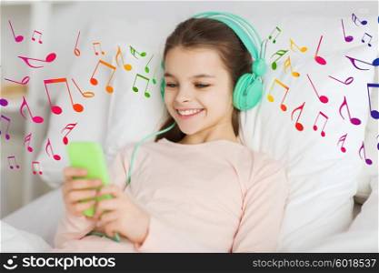 people, children and technology concept - happy smiling girl lying awake with smartphone and headphones in bed listening to music at home over musical notes