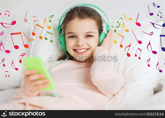 people, children and technology concept - happy smiling girl lying awake with smartphone and headphones in bed listening to music at home over musical notes