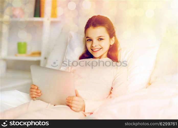 people, children and technology concept - happy smiling girl lying awake with tablet pc computer in bed at home. happy girl lying in bed with tablet pc at home