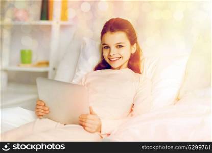 people, children and technology concept - happy smiling girl lying awake with tablet pc computer in bed at home. happy girl lying in bed with tablet pc at home
