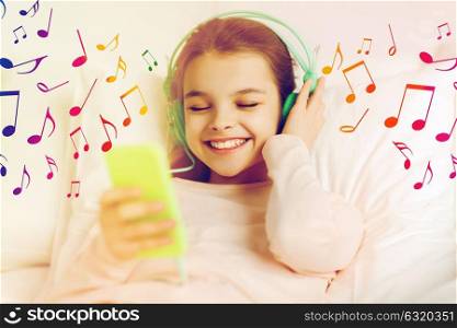 people, children and technology concept - happy smiling girl with smartphone and headphones lying in bed listening to music over musical notes. girl with headphones listening to music in bed