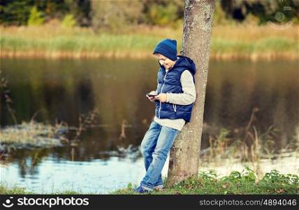 people, children and technology concept - happy teenage boy playing game or texting message on smartphone outdoors