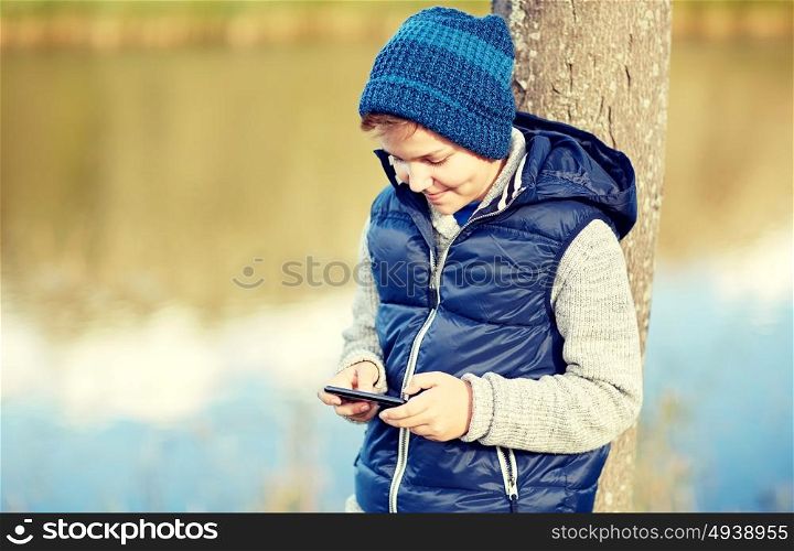 people, children and technology concept - happy teenage boy playing game or texting message on smartphone outdoors. happy boy playing game on smartphone outdoors