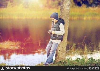 people, children and technology concept - happy teenage boy playing game or texting message on smartphone outdoors. happy boy playing game on smartphone outdoors