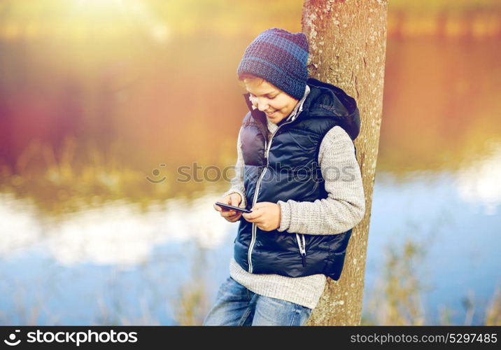 people, children and technology concept - happy teenage boy playing game or texting message on smartphone outdoors. happy boy playing game on smartphone outdoors