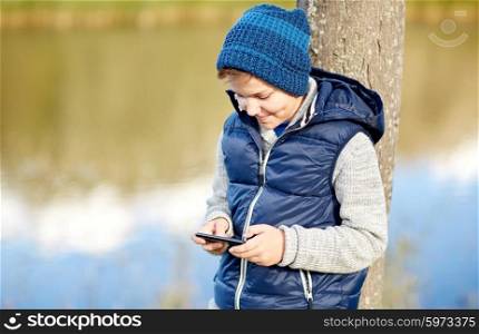 people, children and technology concept - happy teenage boy playing game or texting message on smartphone outdoors