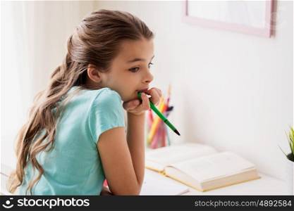 people, children, education and learning concept - bored girl with book and pen doing homework at home