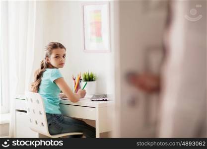 people, children, education and learning concept - girl doing homework at home and mother opens door in her room