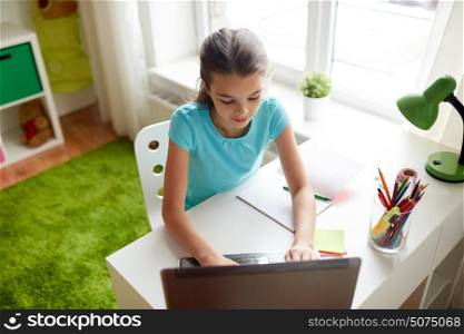 people, children, education and learning concept - happy girl typing on laptop and doing homework at home. happy girl typing on laptop at home