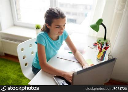 people, children, education and learning concept - happy girl typing on laptop and doing homework at home. happy girl typing on laptop at home