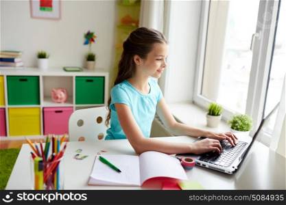 people, children, education and learning concept - happy girl typing on laptop and doing homework at home. happy girl typing on laptop at home. happy girl typing on laptop at home