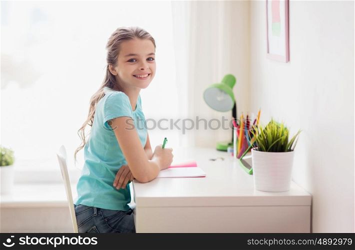 people, children, education and learning concept - happy girl with book writing to notebook at home