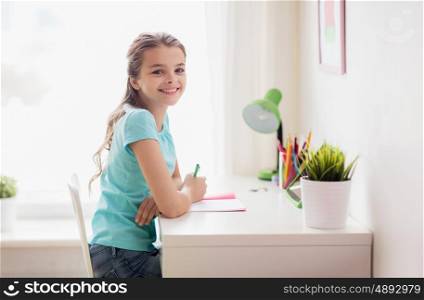 people, children, education and learning concept - happy girl with book writing to notebook at home