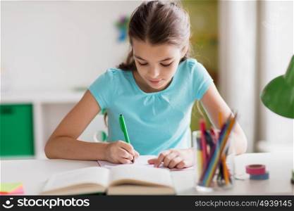people, children, education and learning concept - happy girl with book writing to notebook at home. happy girl with book writing to notebook at home