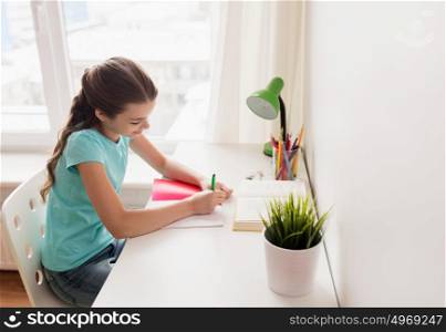 people, children, education and learning concept - happy girl with book writing to notebook at home. happy girl with book writing to notebook at home