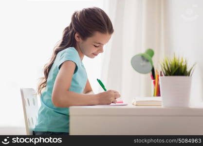 people, children, education and learning concept - happy girl with book writing to notebook at home. happy girl with book writing to notebook at home. happy girl with book writing to notebook at home