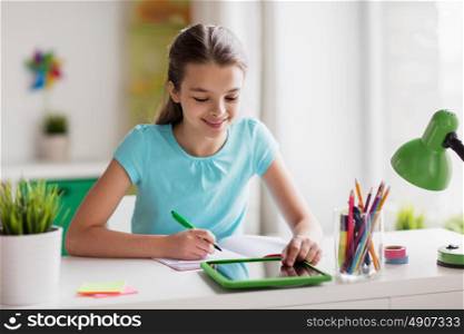 people, children, education and learning concept - happy girl with tablet pc computer writing to notebook at home. girl with tablet pc writing to notebook at home