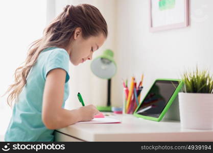 people, children, education and learning concept - happy girl with tablet pc computer writing to notebook at home. girl with tablet pc writing to notebook at home