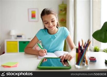 people, children, education and learning concept - happy girl with tablet pc computer writing to notebook at home. girl with tablet pc writing to notebook at home