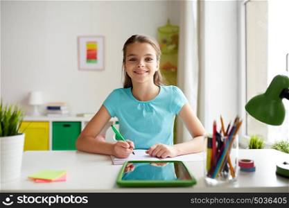 people, children, education and learning concept - happy smiling girl with tablet pc computer and notebook doing homework at home. happy girl with tablet pc and notebook at home