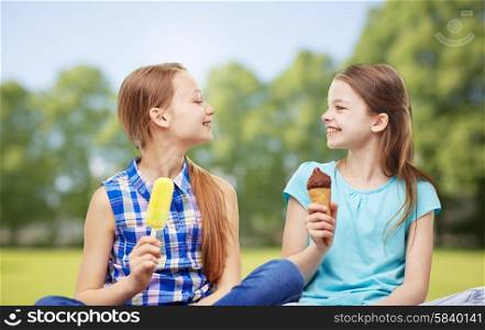 people, children, friends and friendship concept - happy little girls eating ice-cream over summer park background