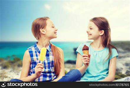 people, children, friends and friendship concept - happy little girls eating ice-cream over summer beach background