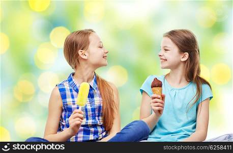 people, children, friends and friendship concept - happy little girls eating ice-cream over green holidays lights background