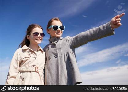people, children, friends and friendship concept -happy little girls in sunglasses hugging and pointing finger outdoors