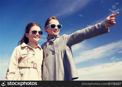 people, children, friends and friendship concept -happy little girls in sunglasses hugging and pointing finger outdoors