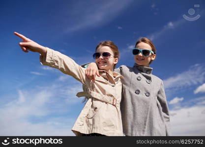 people, children, friends and friendship concept -happy little girls in sunglasses hugging and pointing finger outdoors