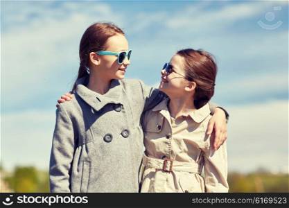 people, children, friends and friendship concept - happy little girls in sunglasses hugging and talking outdoors
