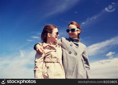 people, children, friends and friendship concept - happy little girls in sunglasses hugging and talking outdoors