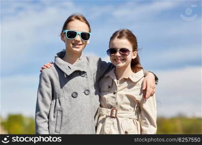people, children, friends and friendship concept - happy little girls in sunglasses hugging outdoors