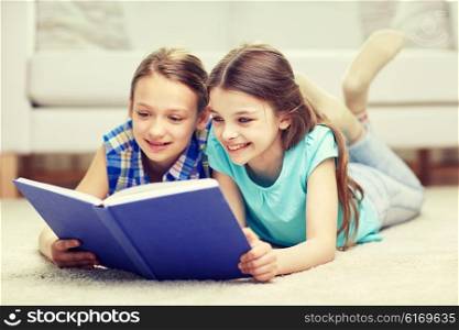 people, children, friends, literature and friendship concept - two happy girls lying on floor and reading book at home