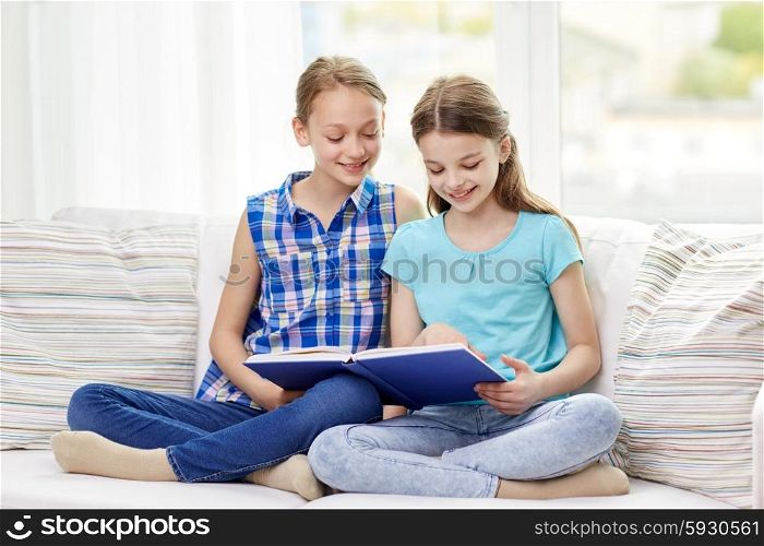 people, children, friends, literature and friendship concept - two happy girls sitting on sofa and reading book at home